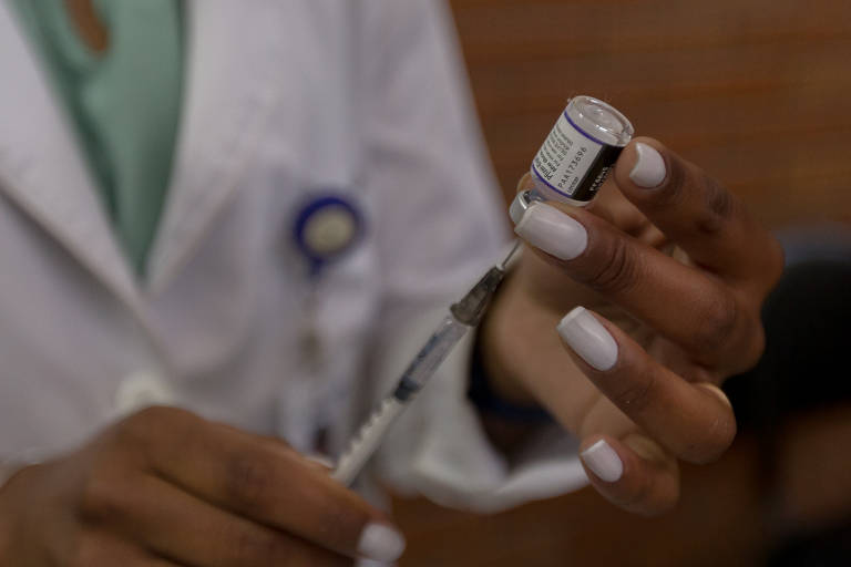 Profissional da saúde espeta uma seringa em uma ampola de vacina contra a Covid da Pfizer