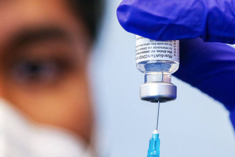 Imagem em close mostra profissional da saúde espetando uma seringa em uma ampola de vacina