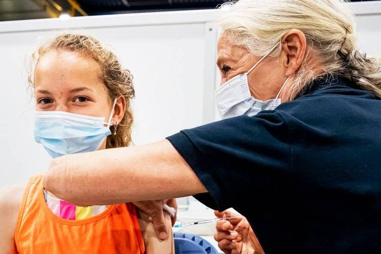 Menina de máscara recebe vacina de um profissional da saúde
