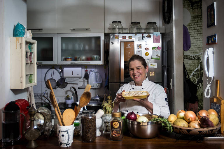 Sonia Schwartz, 52 anos, sorri e segura embalagem com comida em sua cozinha. Ela faz comida em casa para vender e acredita que seu negócio será impactado com a alta da luz