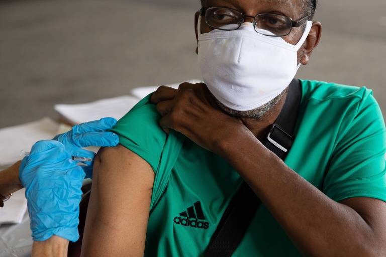 Imagem em primeiro plano mostra homem negro de máscara sendo vacinado.