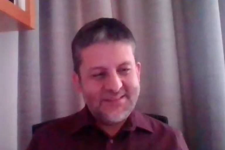Imagem de reprosução mostra Ricardo Palacios em vídeo chamada. Ele usa camisa e sorri