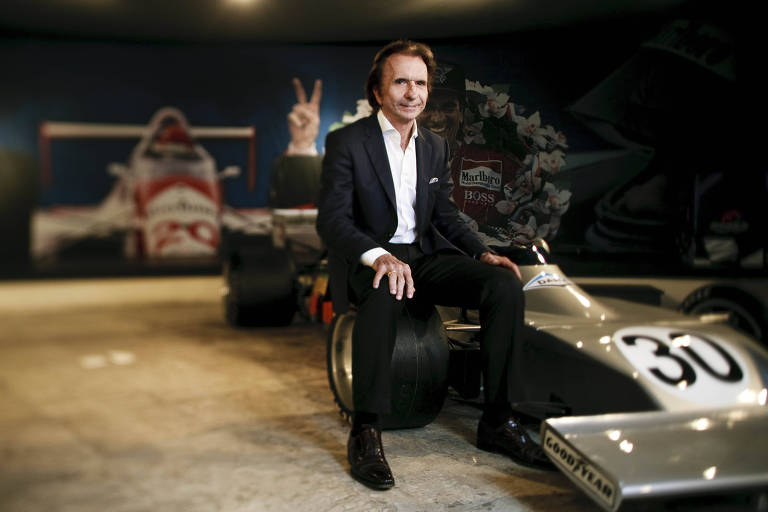 Emerson Fittipaldi posa para foto sentado ao lado de carro de fórmula 1