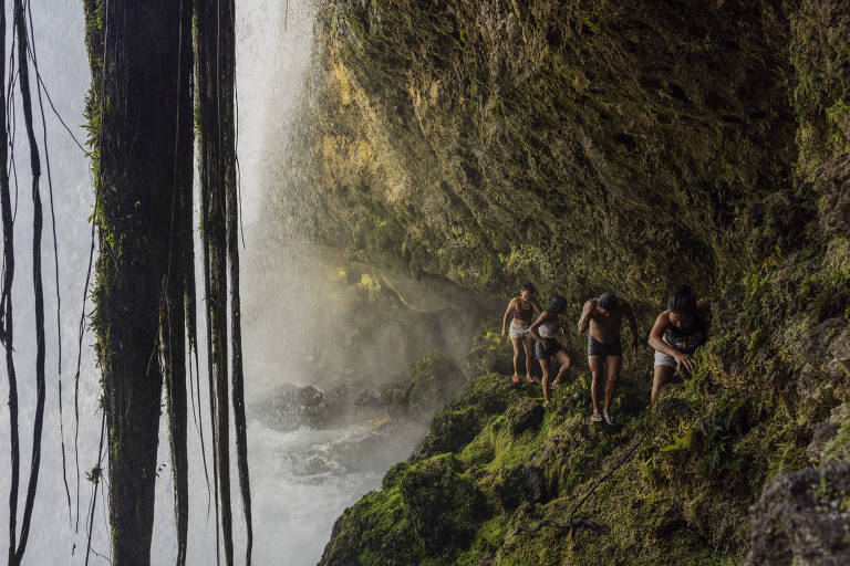Jovens manokis atravessam por baixo de uma cachoeira o rio Cravari, na Terra Indígena Irantxe