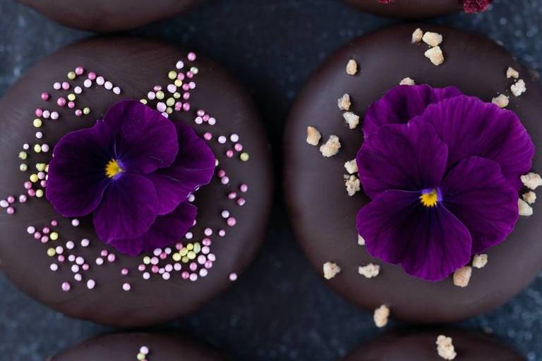 Bolos com cobertura preta confeitados com granulado colorido e flores comestíveis violetas