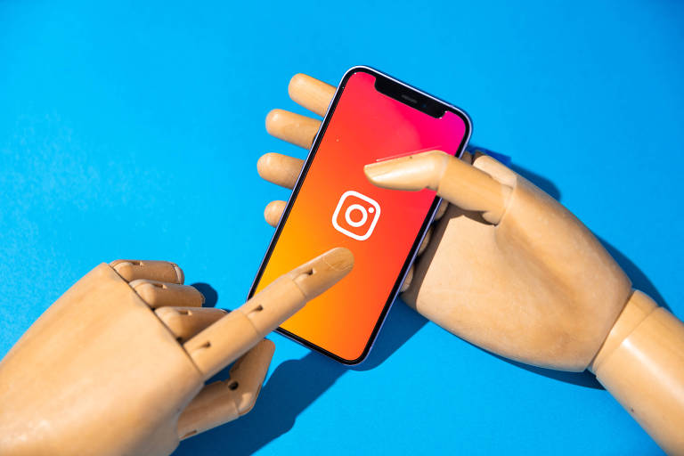 Mão de manequim de madeira toca tela de smartphone carregando aplicativo do Instagram