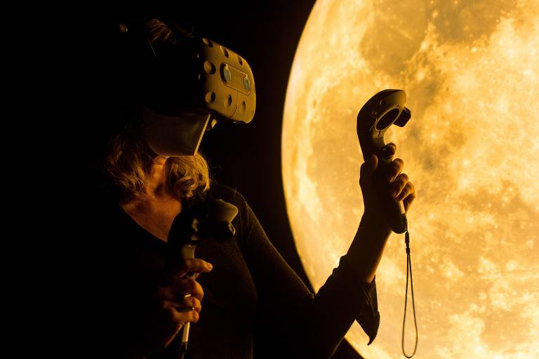 Mulher usa óuclos de realidade virtual enquanto usa controles para se guiar e, ao fundo, há uma imagem de uma lua iluminada