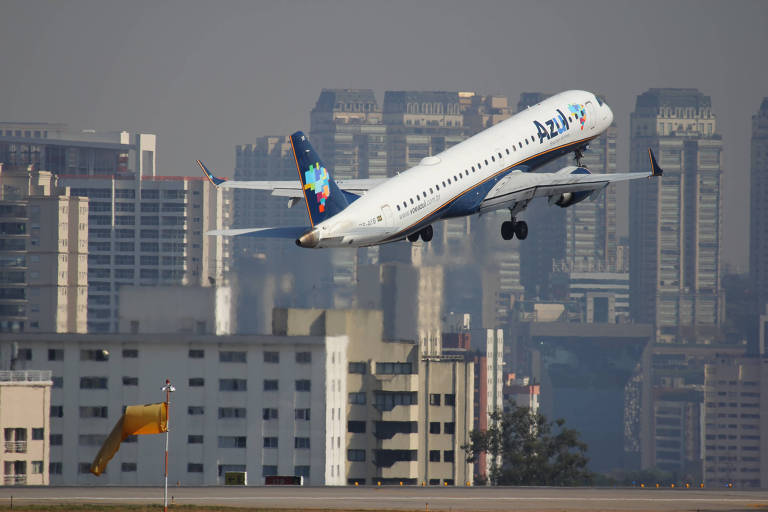 Imagem mostra um avião da Azul Linhas Aéreas decolando. Ao fundo, se vê prédios.