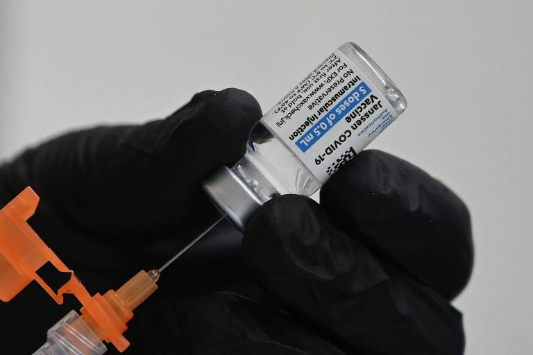Mão segura agulha e injeção, puxando o líquido da vacina da Janssen de dentro de um frasco