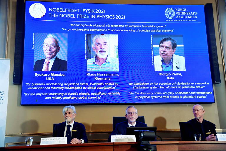 Em destaque, em um telão aparece a fotografia dos pesquisadores Syukuro Manabe, Klaus Hasselmann e Giorgio Parisi, vencedores do Nobel de Física