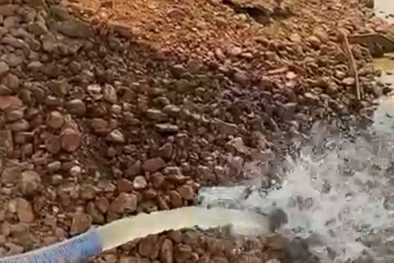 Uma mangueira joga água em um solo de pedras