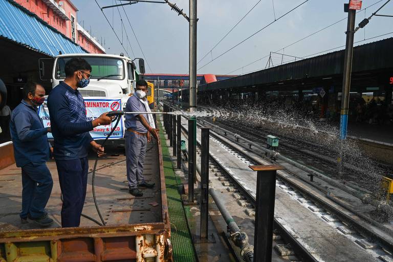 homens vestidos de azul escuro seguram mangueira que jorra liquido em trilhos de trem