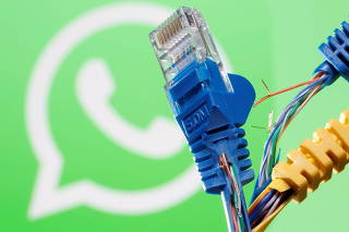 Broken Ethernet cables are seen in front of a displayed WhatsApp logo in this illustration