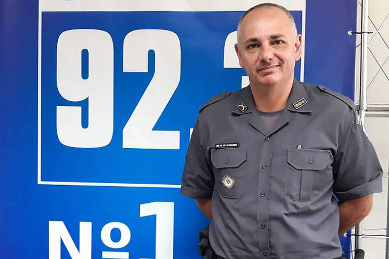 Um policial calvo, fardado, diante de um fundo azul com o número de uma rádio