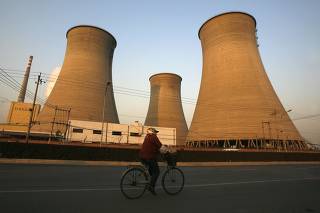 Woman rides her bicycle past cooling towers at a coal-burning power station in Beijing