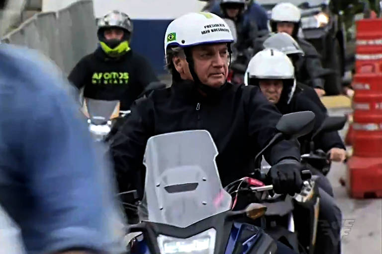 Bolsonaro está de casaco preto, dirigindo uma moto. Seu capacete é aberto nas laterais e no queixo