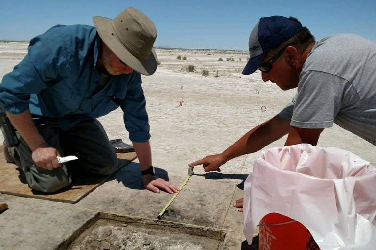 Imagem mostra dois homens abaixados trabalhando em um sítio arqueológico