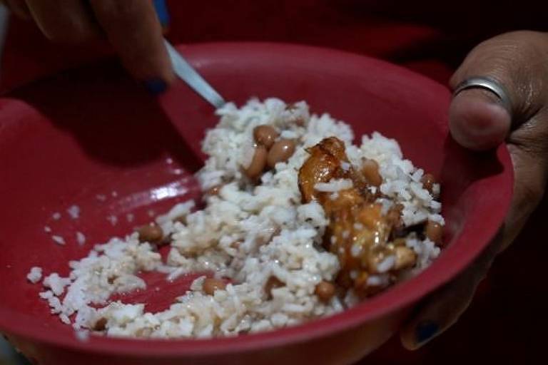 Prato vermelho com arroz branco, feijão marrom claro, carcaças e pele de frango