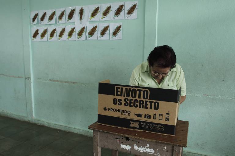 Eleitora vota em zona eleitoral em San Jose, capital da Costa Rica; na urna está escrito 'o voto é secreto'