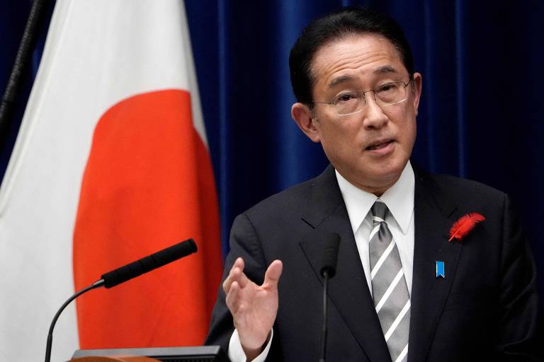Primeiro-ministro japonês fala em microfone em frente à bandeira do Japão