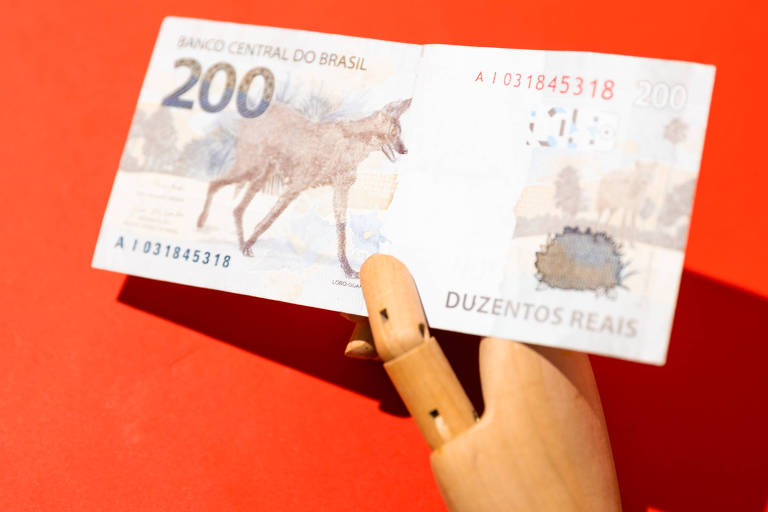 Imagem mostra mão de madeira segurando cédula de R$ 200