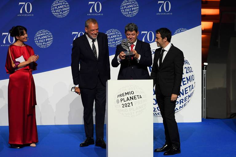 Três homens de terno recebem um troféu
