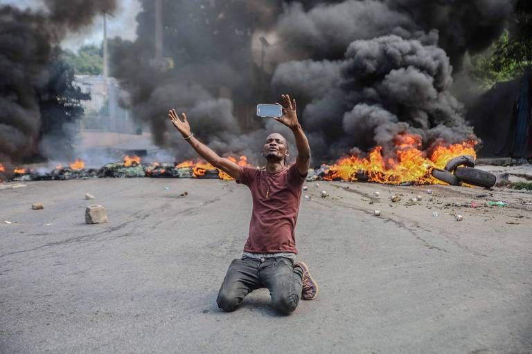 Homem filma a si mesmo próximo a pneus pegando fogo, durante a greve geral para denunciar a insegurança em Porto Príncipe 
