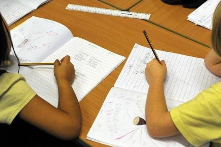 Duas crianças que compatilham de uma mesma mesa escrevem em um caderno
