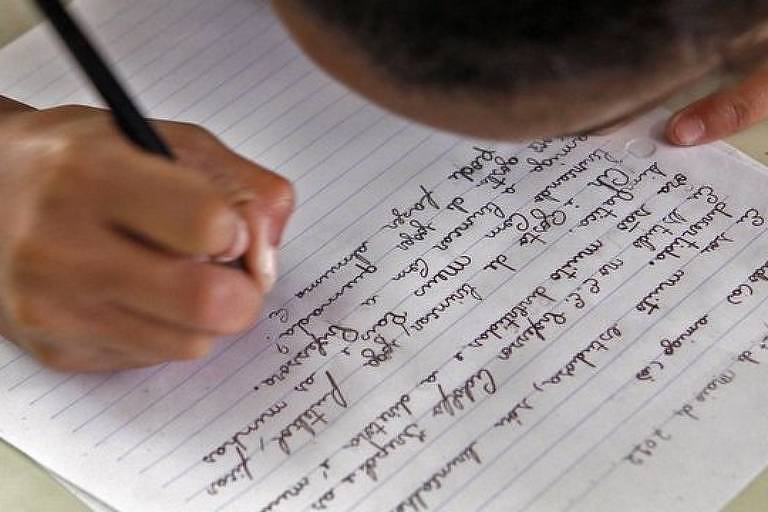 Imagem em close mostra a mão de uma criança escrevendo em uma folha de papel
