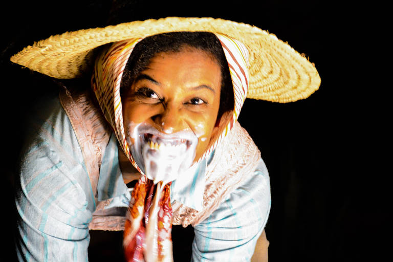 Uma mulher negra com chapéu de palha e espuma branca na boca