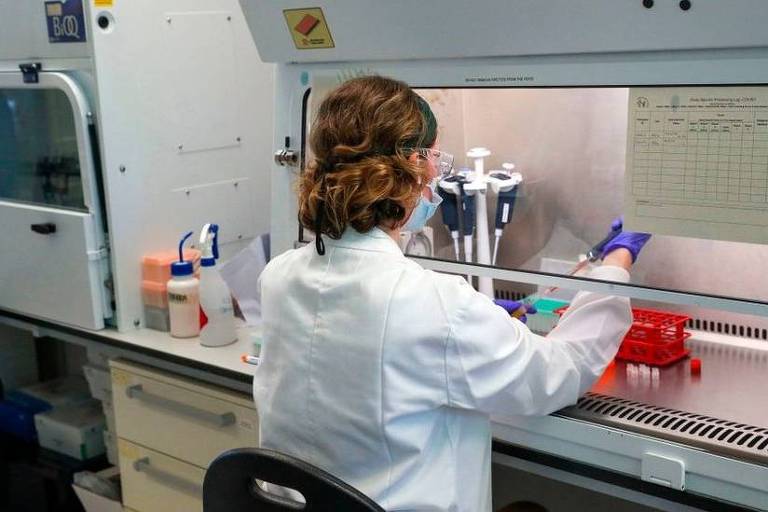 Em um laboratório, uma mulher está de costas manuseando equipamentos de pesquisa
