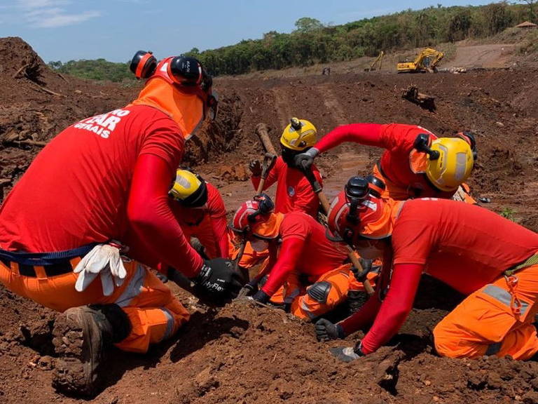 A foto mostra um grupo de bombeiros agachados remexendo a terra com equipamentos em busca de corpos de vítimas do rompimento de barragem da Vale em Brumadinho (MG)