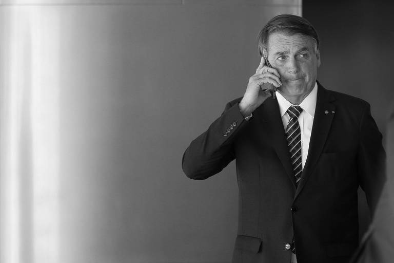 Homem de meia idade de terno escuro, camisa branca e gravata escura listrada, falando ao telefone celular.
