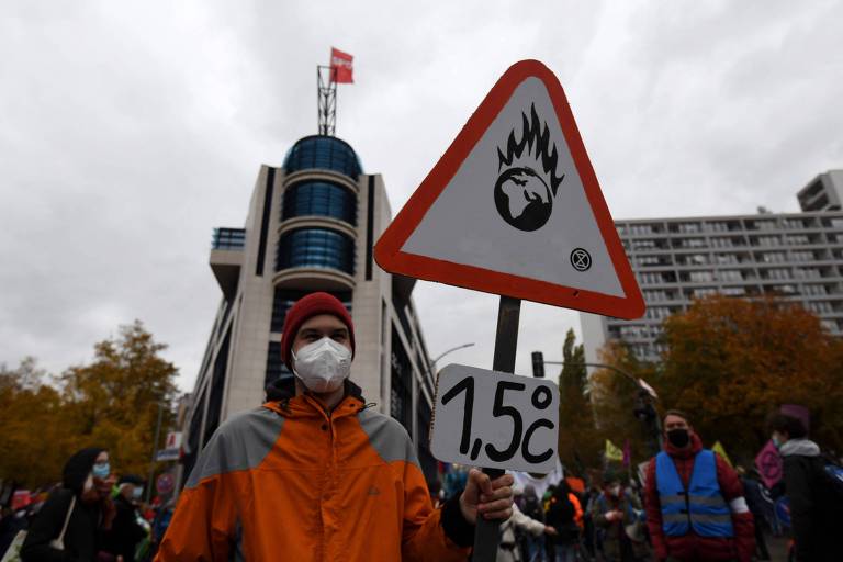 Ativista segura cartaz mostrando planeta que faz referência ao Acordo de Paris de 2015, para limitar o aquecimento global a 1,5°C