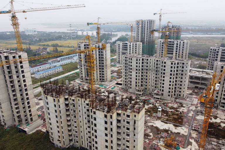 Vista aérea de um complexo de edifícios em construção, à beira de um rio.