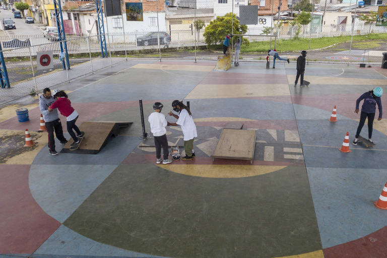 Foto aberta de crianças sendo orientadas perto de obstáculos montados numa quadra poliesportiva