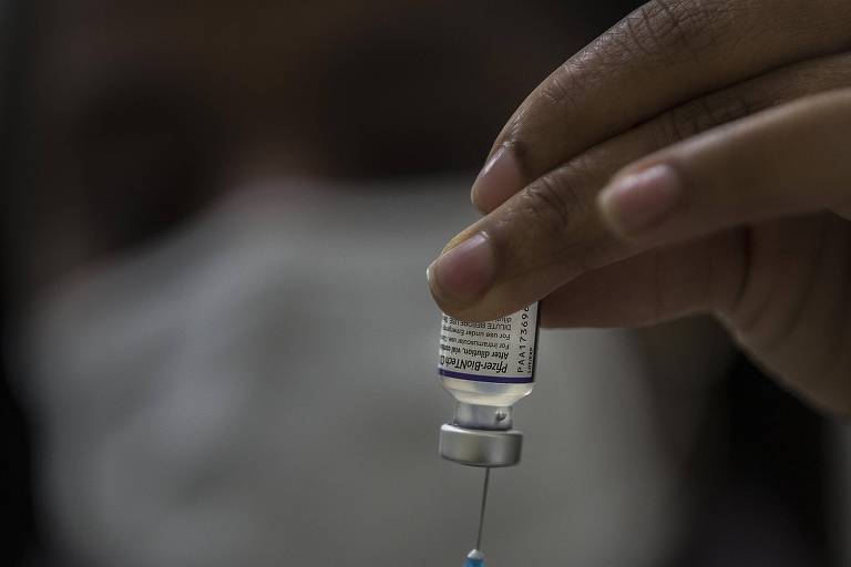 Imagem em close mostra profissional da saúde espetando uma seringa em uma ampola de vacina