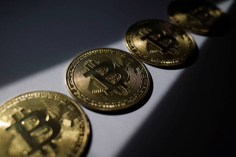 Fotografia mostra quatro moedas douradas enfileiradas; elas tem grafado um "B" de bitcoin