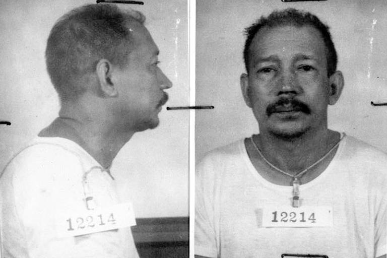 Fotos de frente e perfil de homem de meia idade, de cabelos ralos e bigode, vestido com uma camiseta branca. As fotos são do seu prontuário policial