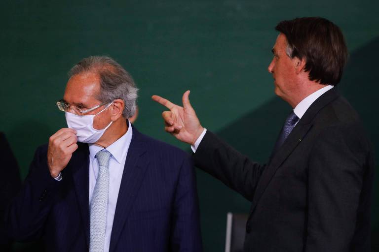 O ministro Paulo Guedes (esq) ao lado do presidente Bolsonaro, fazendo um gesto de arma com a mão