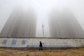 FILE PHOTO: Woman wearing a mask walks past buildings on a polluted day in Hebei