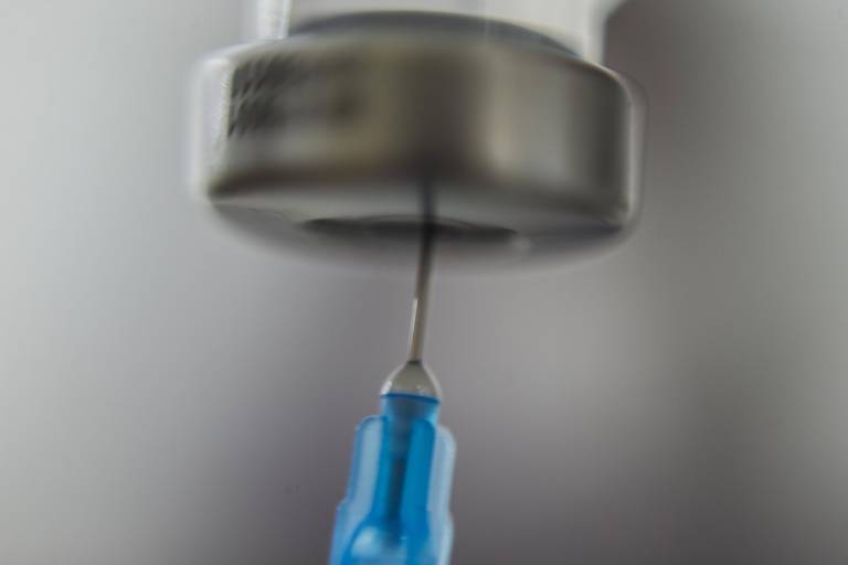 Detalhe de agulha entrando em frasco com vacina
