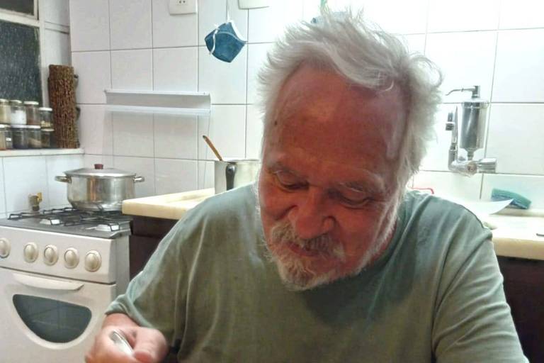 um homem idoso está sentado de frente para uma mesa segurando um garfo e olhando para um prato de comida.