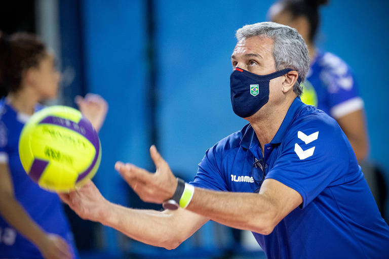 Zé Roberto, de camiseta azul e máscara, com os braços preparados para segurar uma bola amarela
