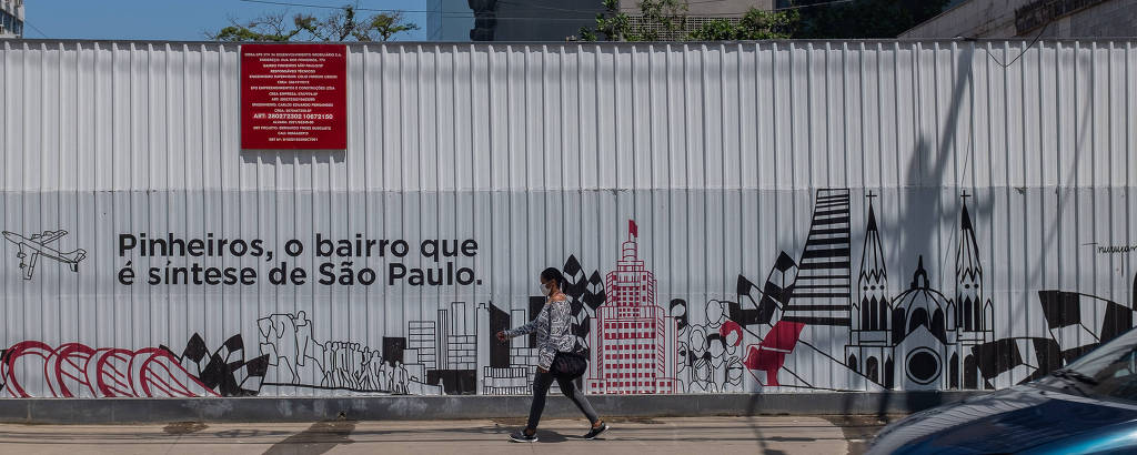 Pedestre passa em frente à tapume de prédio em construção na rua dos Pinheiros no qual se lê a frase 