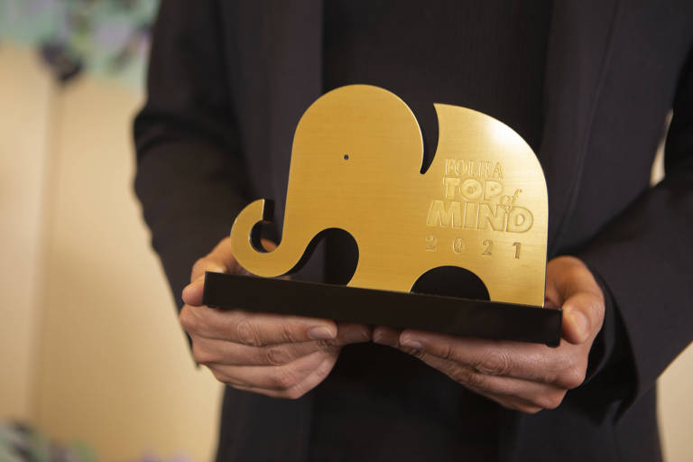 imagem mostra troféu dourado em formato de elefante. Ele está nas mãos de um homem, que veste um terno preto.