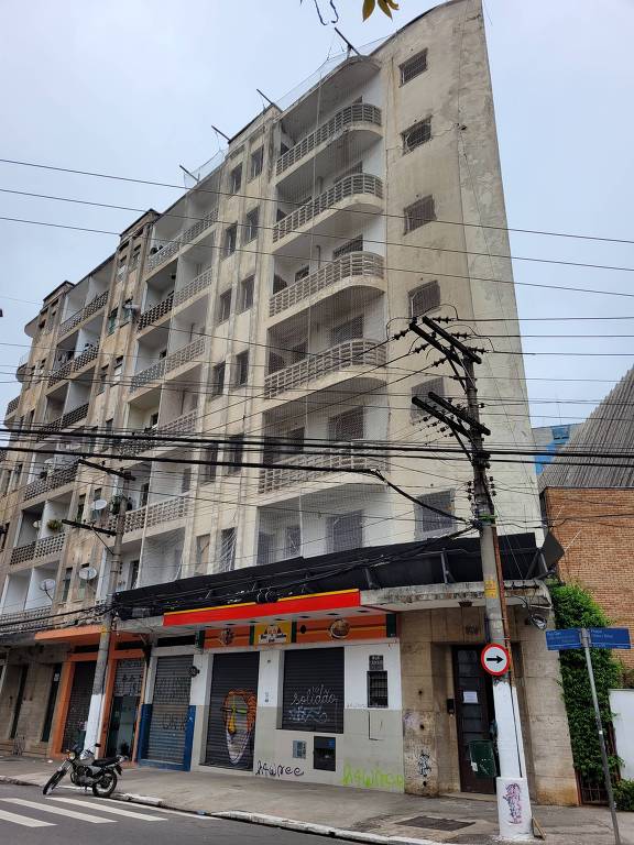 Fachada de prédio cinza, deteriorado, com rede de proteção 