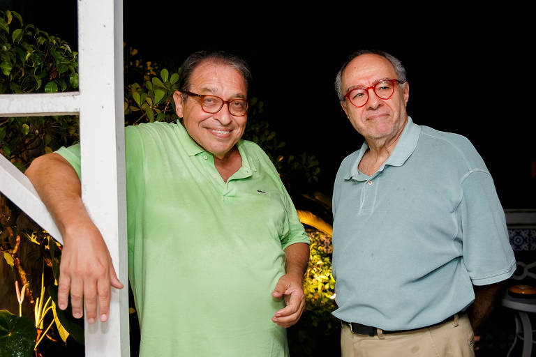 A foto apresenta, em primeiro plano, da cintura para cima, o escritor e colunista da Folha Ruy Castro e jornalista e escritor Sérgio Augusto, no Rio, em 2018. Ambos usam óculos com aros em cor vinho, vestem camisas pólos, Ruy na cor verde e Sérgio na cor azul. 