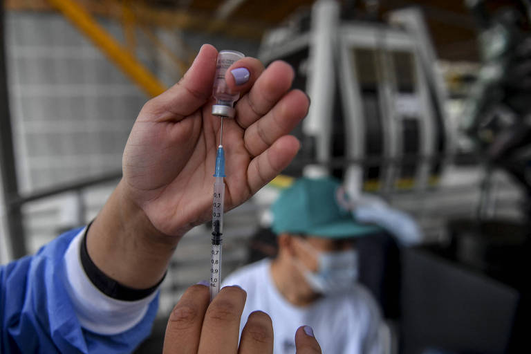 Profissional da saúde espeta uma seringa em uma ampola de vacina