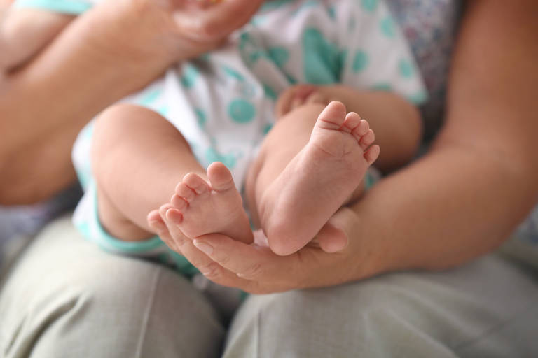 Close nas solas dos pés de um bebê branco que está deitado sobre uma mulher sentada
